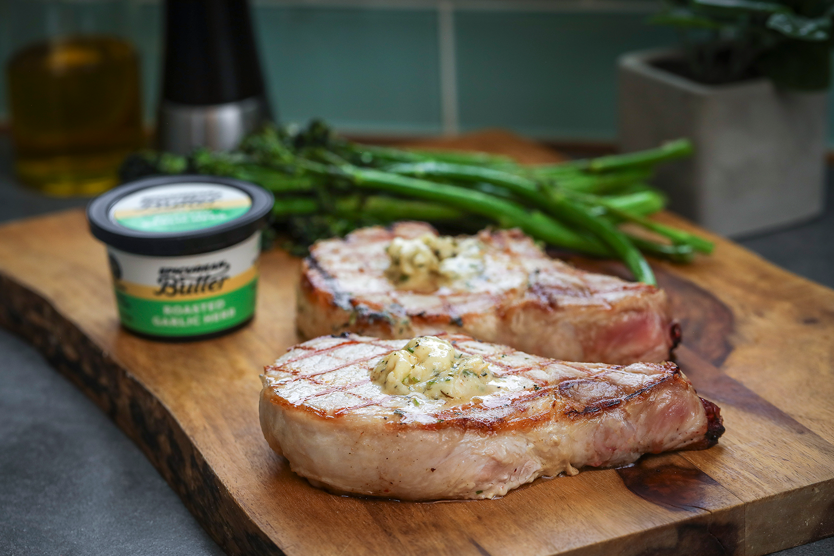 Pork chops topped with Epicurean Butter Roasted Garlic Herb Flavored Butter, served with roasted broccolini